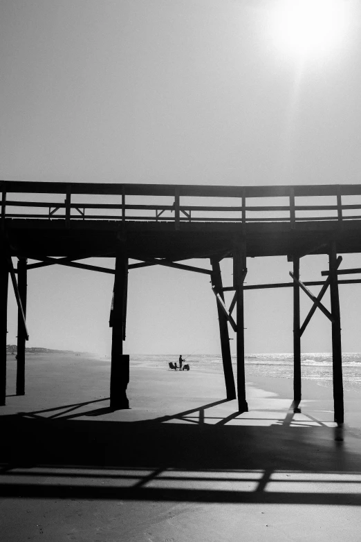 black and white image of a man sitting on a chair under a pier