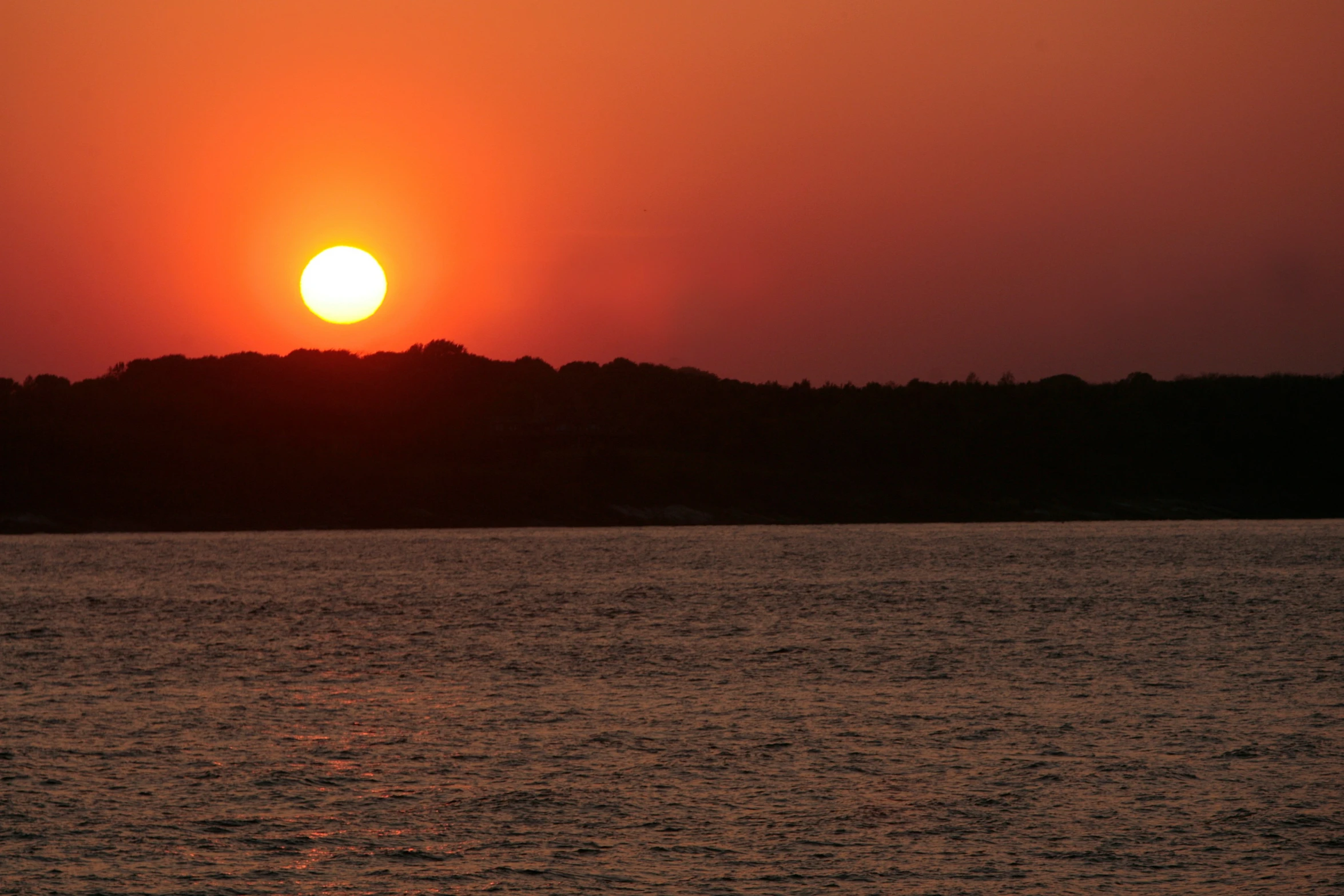 the sun setting over some trees on a large body of water