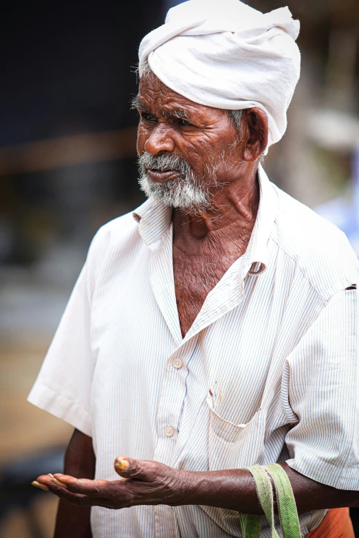 an old man in white shirt and turban standing with a pipe