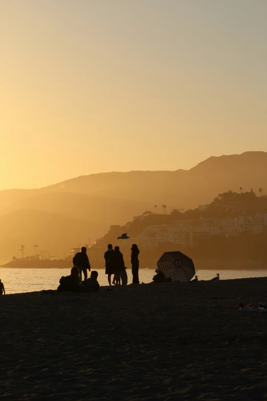 several people on the beach at sunset with the town in the distance