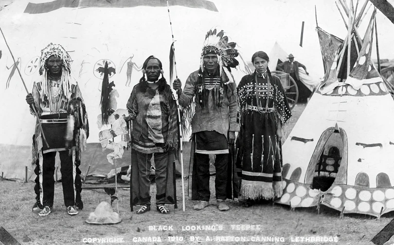 four indians with large spears stand in front of an indian teepee