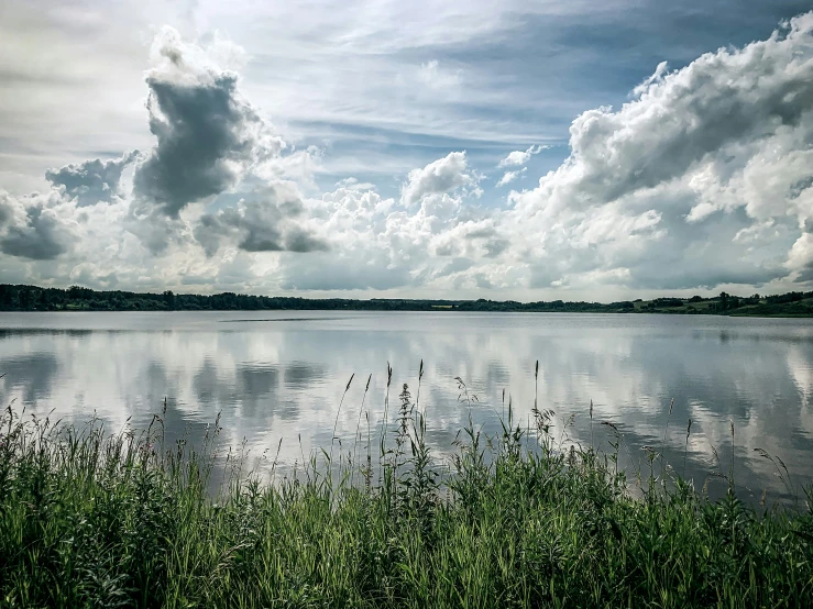 the sky is getting dark and cloudy and the water in front of it has plants and grass on the side of it