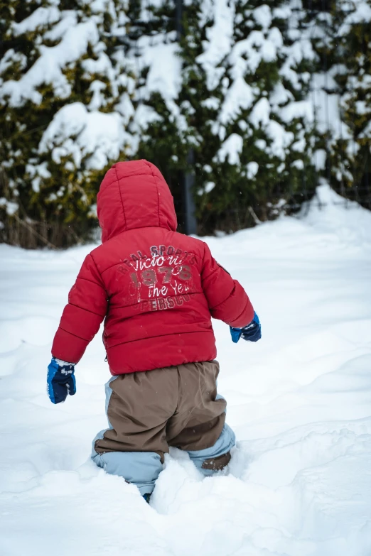 a toddler stands in deep snow with his feet up in the air