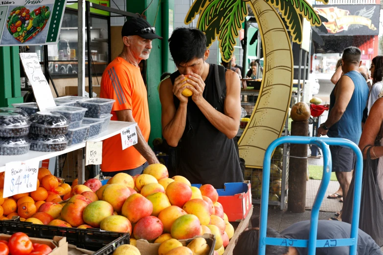 two people standing next to some fruit outside