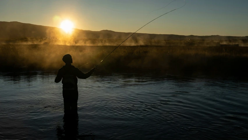 a man is fishing in the river at sunset