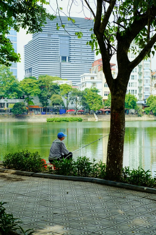 a man sitting in front of a lake with the cityscape behind him