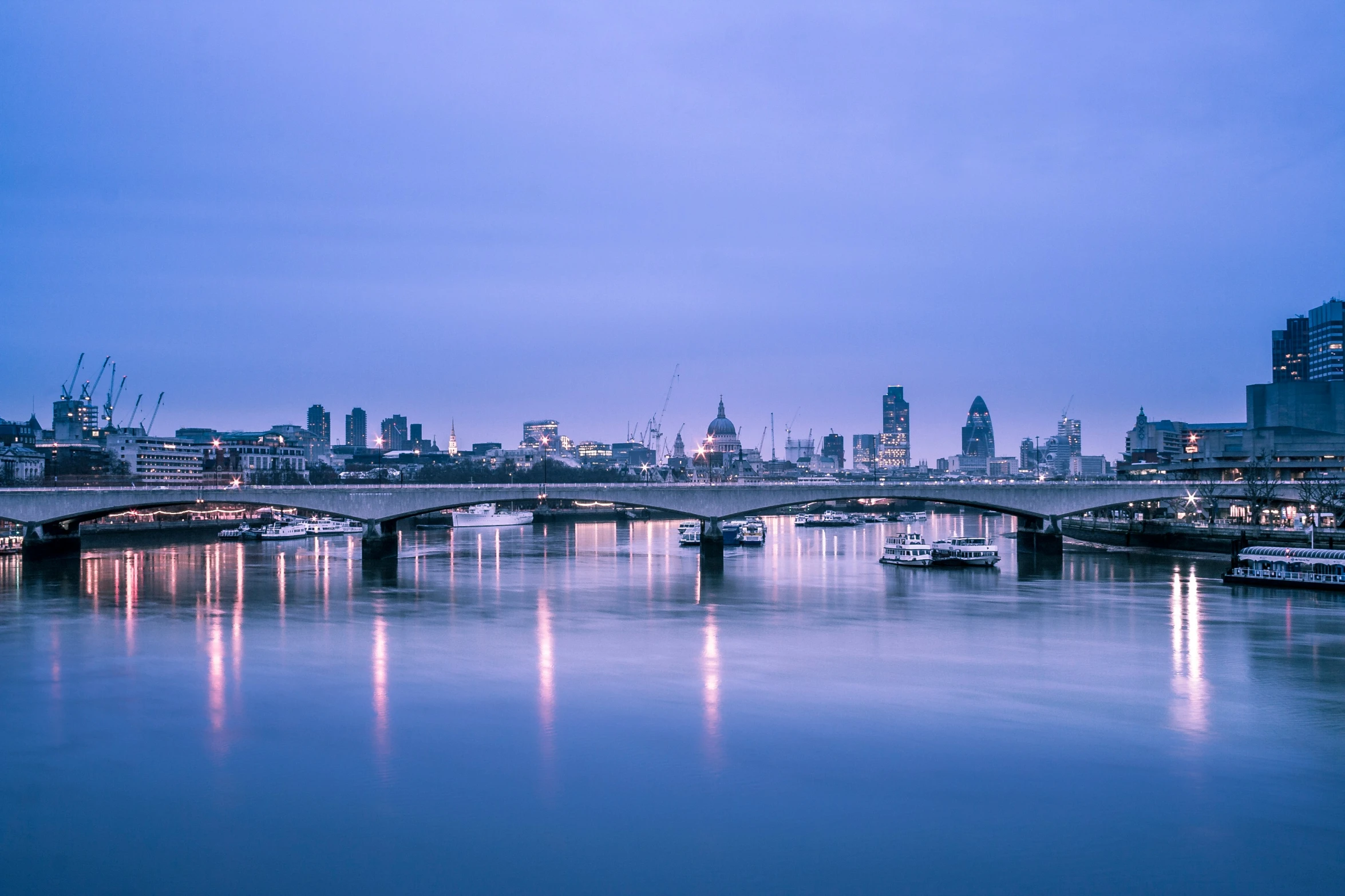 a cityscape is pictured in the dusk as the water flows underneath