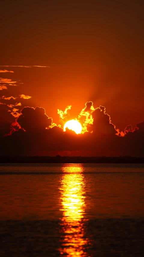 an orange and red sky with dark clouds reflected in water