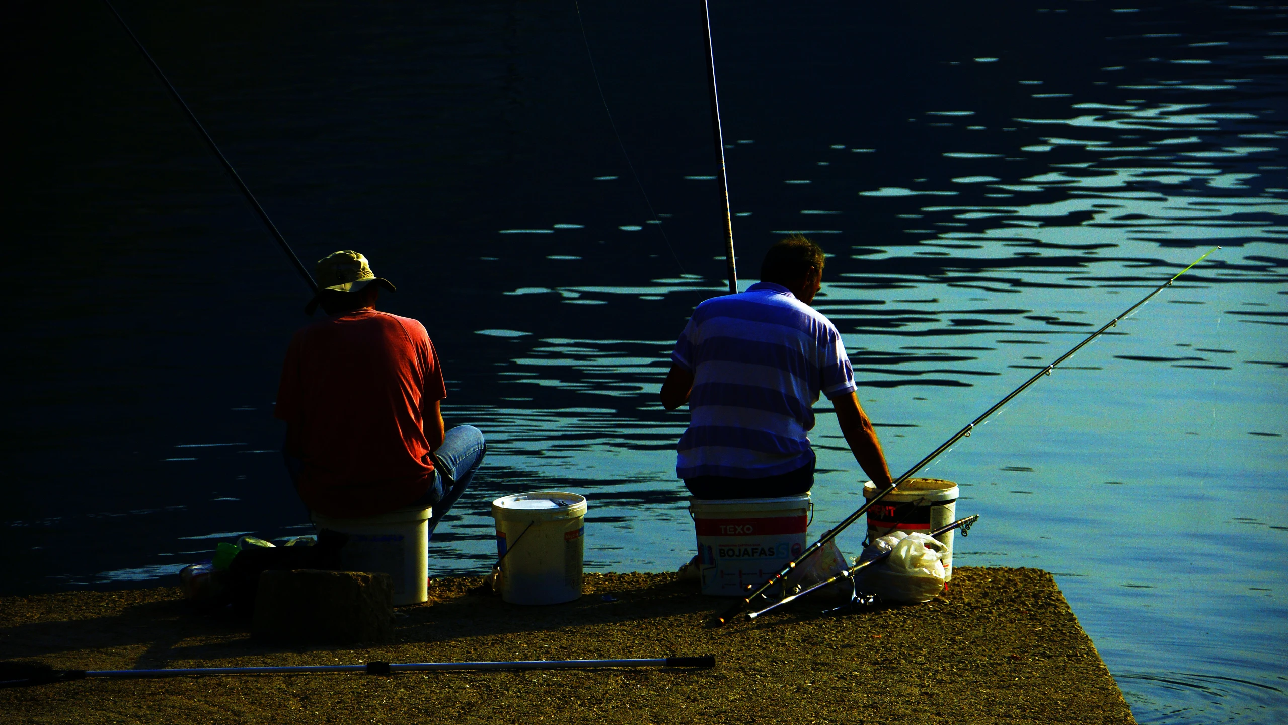 two men fishing on a dock at the water