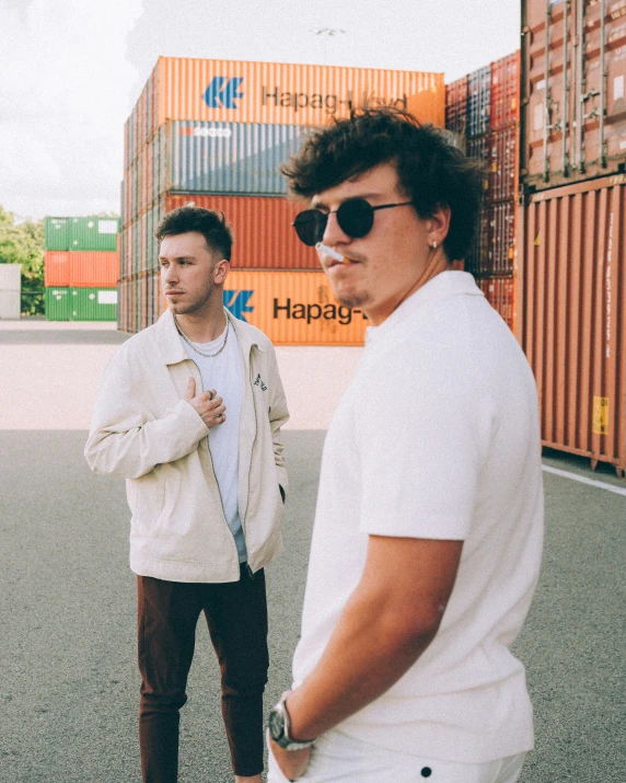 two men standing next to each other near shipping containers