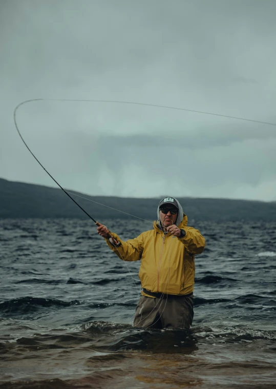 a man with a yellow coat and black hat on is holding a fishing pole