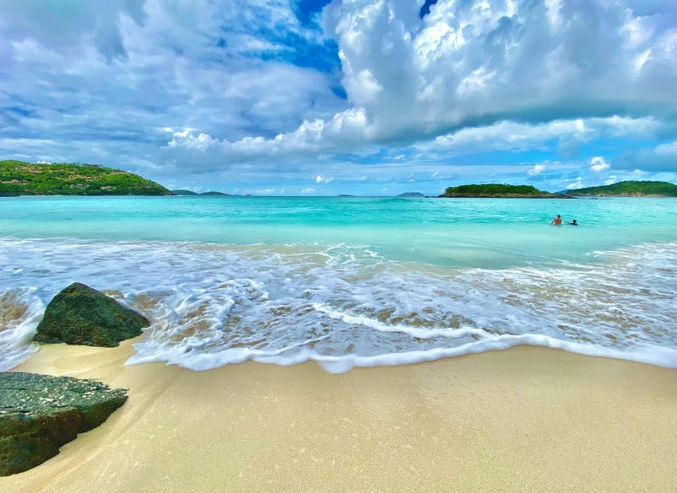 beach scene with waves coming in and two people swimming