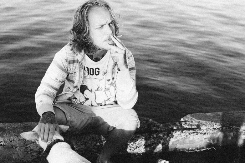 a woman sitting on the edge of a lake with her hand near her mouth