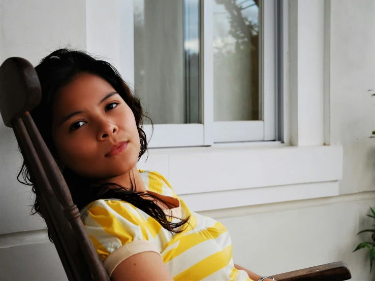 a girl in a striped shirt sitting on a porch chair