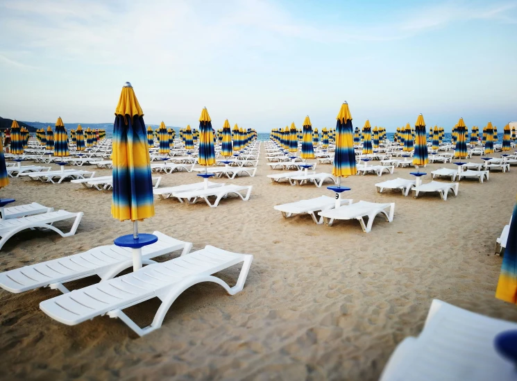 large number of white beach chairs with yellow and blue umbrellas