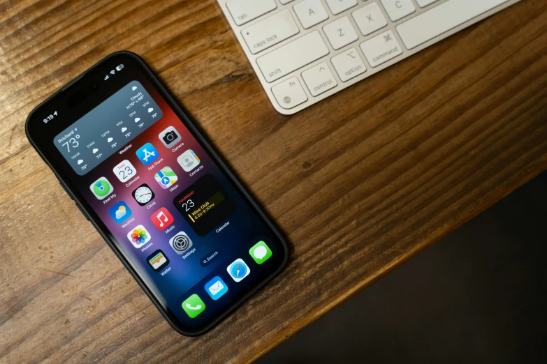 a phone laying next to a keyboard on a wooden table