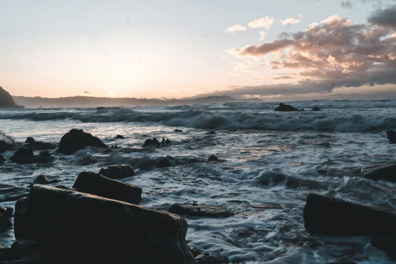 a cloudy sunrise over the ocean next to rocks and water