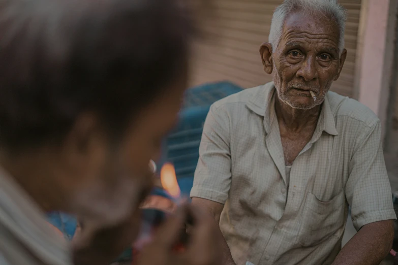 a man sitting down smoking soing and holding his cigarette in one hand