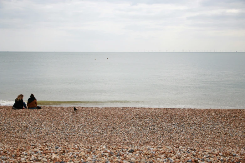 two people sitting on the beach watching the water