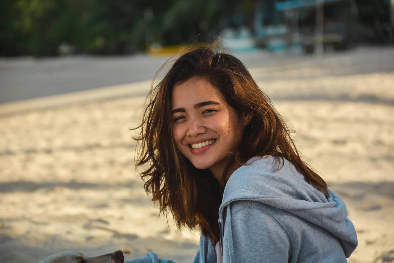 a woman smiles while holding a dog on a beach