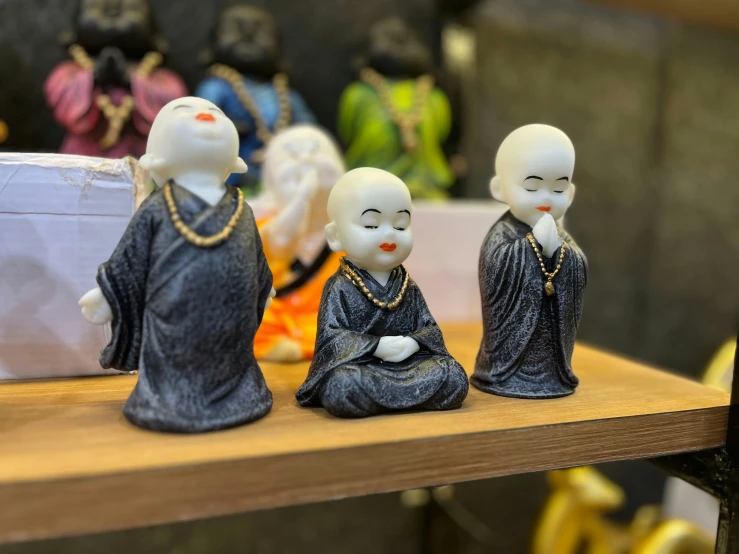 a set of three ceramic monk statues on top of a wooden table