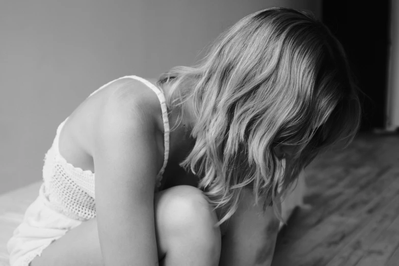 black and white image of young woman sitting on bed