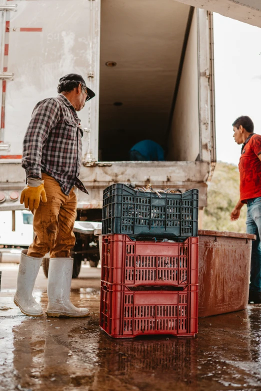 two men stand in a barnyard with red crates