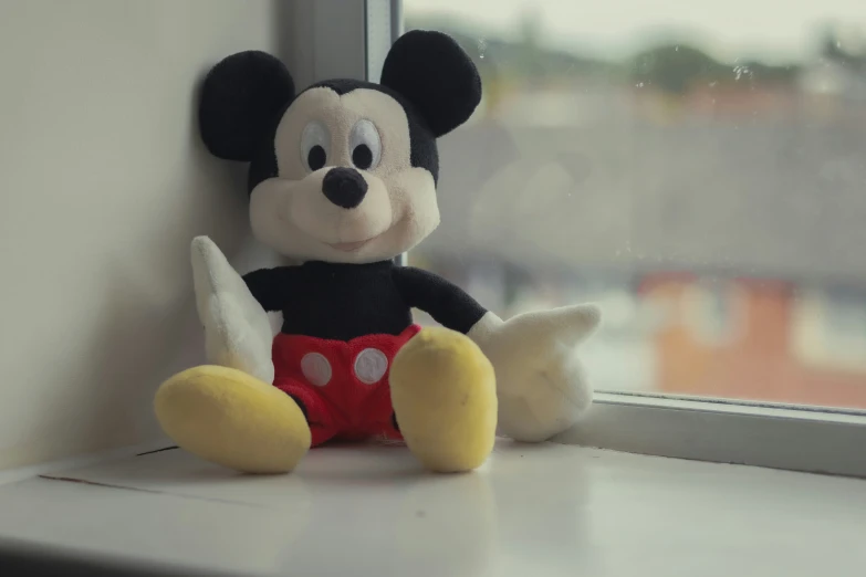 a mickey mouse stuffed toy sits on a window sill