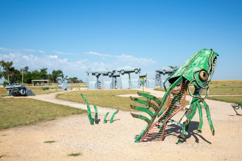 an upside down sculpture of a green mantisbee on gravel