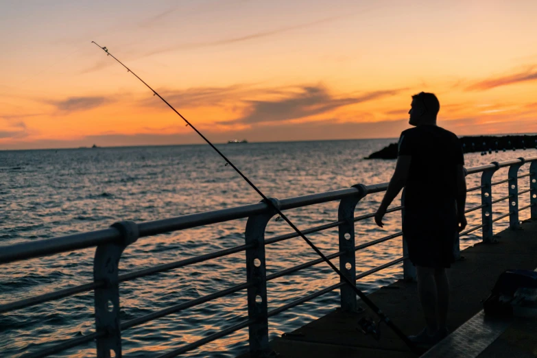 a man is fishing on the pier at sunset