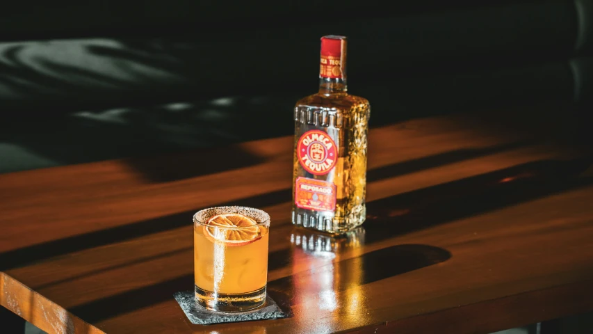 a bottle and a glass with some orange in it on a table