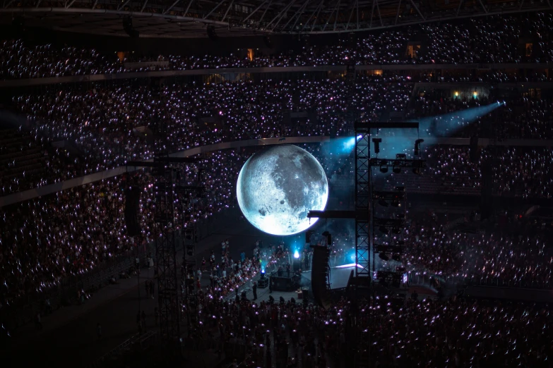 the moon appears to float on stage in the middle of the stadium