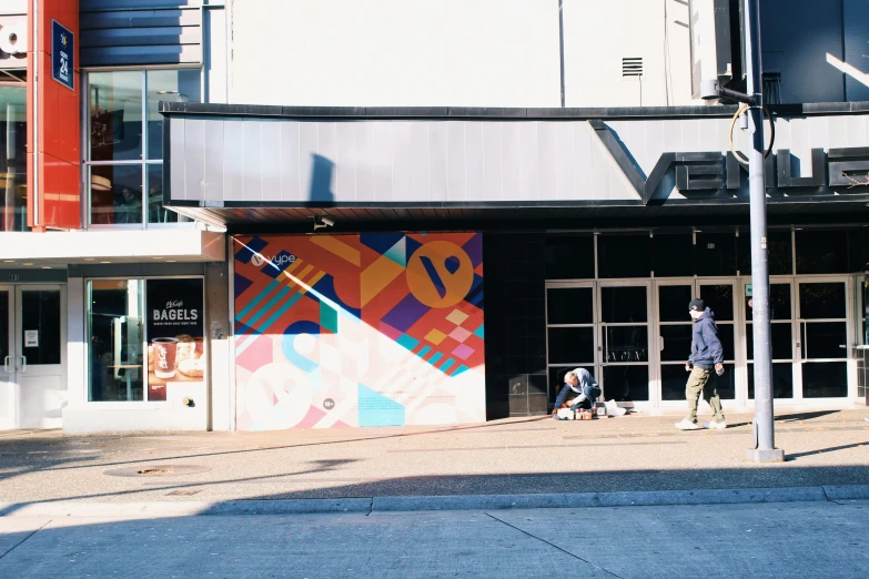 people on a city street near a building with large graffiti