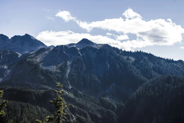 a mountain top with pine trees and a sky filled with clouds