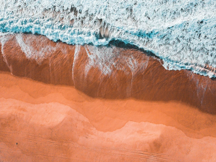 red sand and waves are seen from above