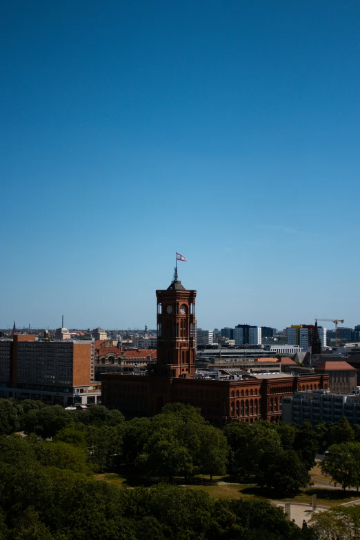 the tall clock tower of the university has a flag flying atop it