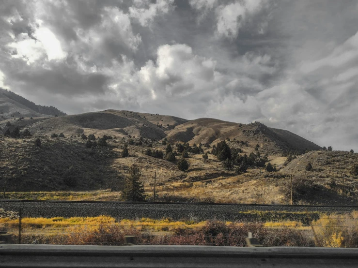 a field near some mountains under a cloudy sky