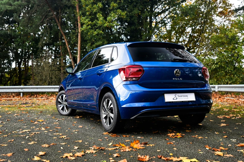 a bright blue car sits parked in the fall leaves