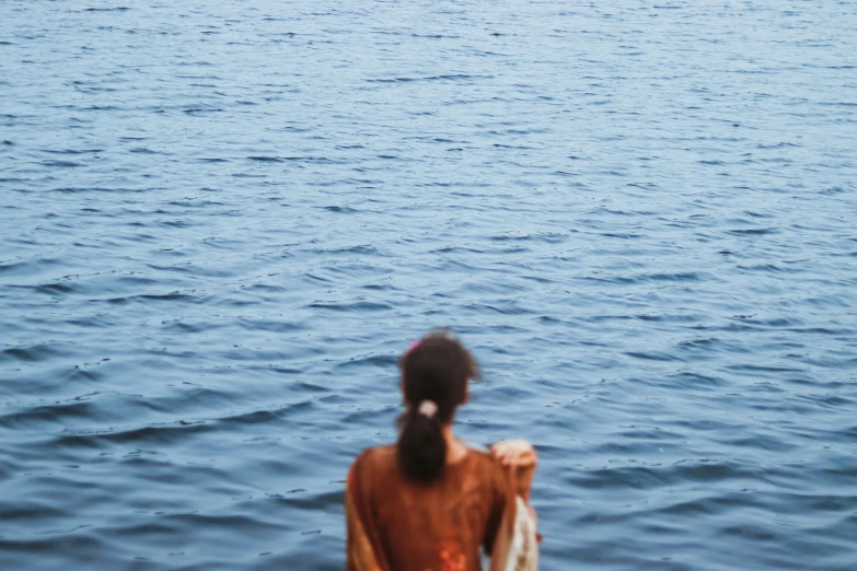 a woman standing in the middle of the ocean looking at a flying kite