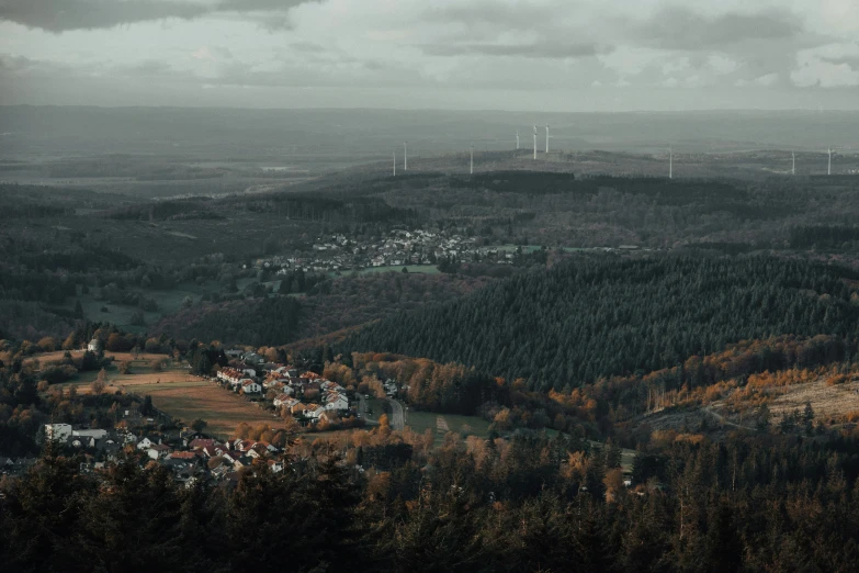 a valley with a town on the hill, and wind turbines in the distance