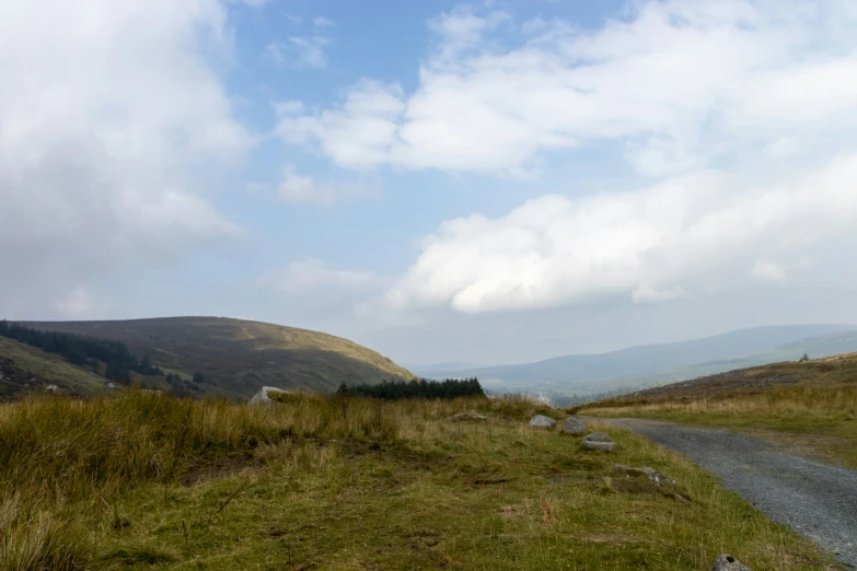 an empty paved road going between a grassy hillside and a hill