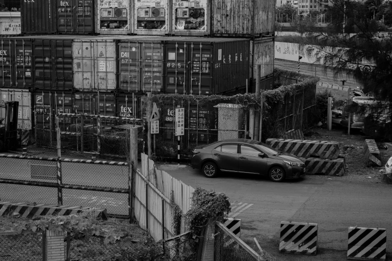 car in parking lot in front of a large stack of shipping containers