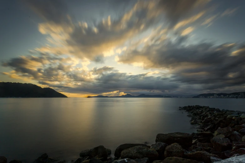 a rocky shore and blue water under cloudy skies