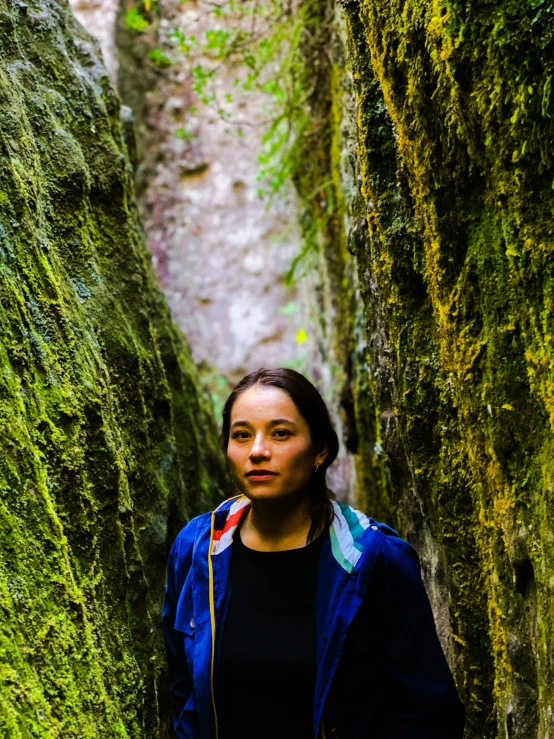 a young woman standing on the trail between moss covered rocks