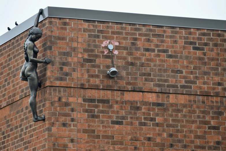 statue of woman with hands raised, bird on brick building