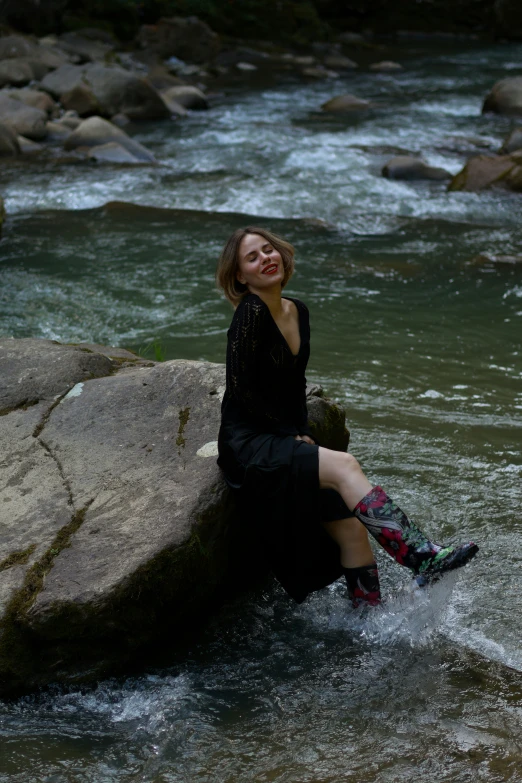 a woman sitting on a rock in water near rocks