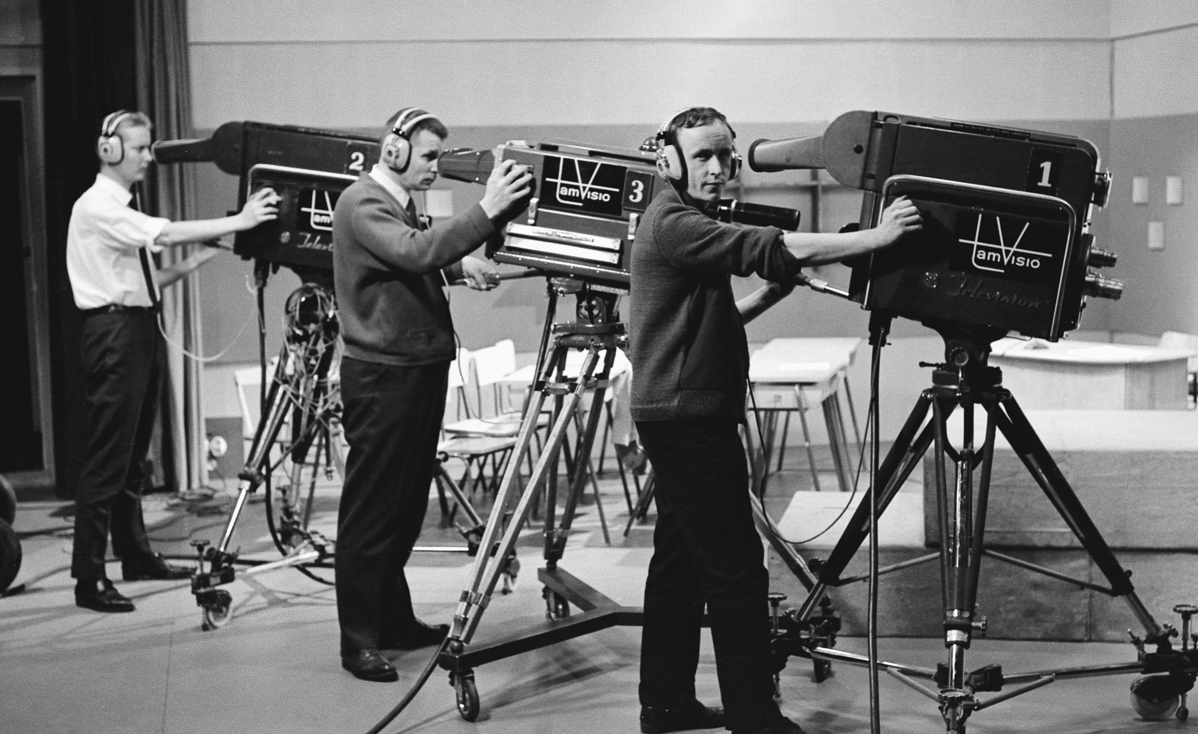 men stand near movie projectors while one looks at soing on the camera