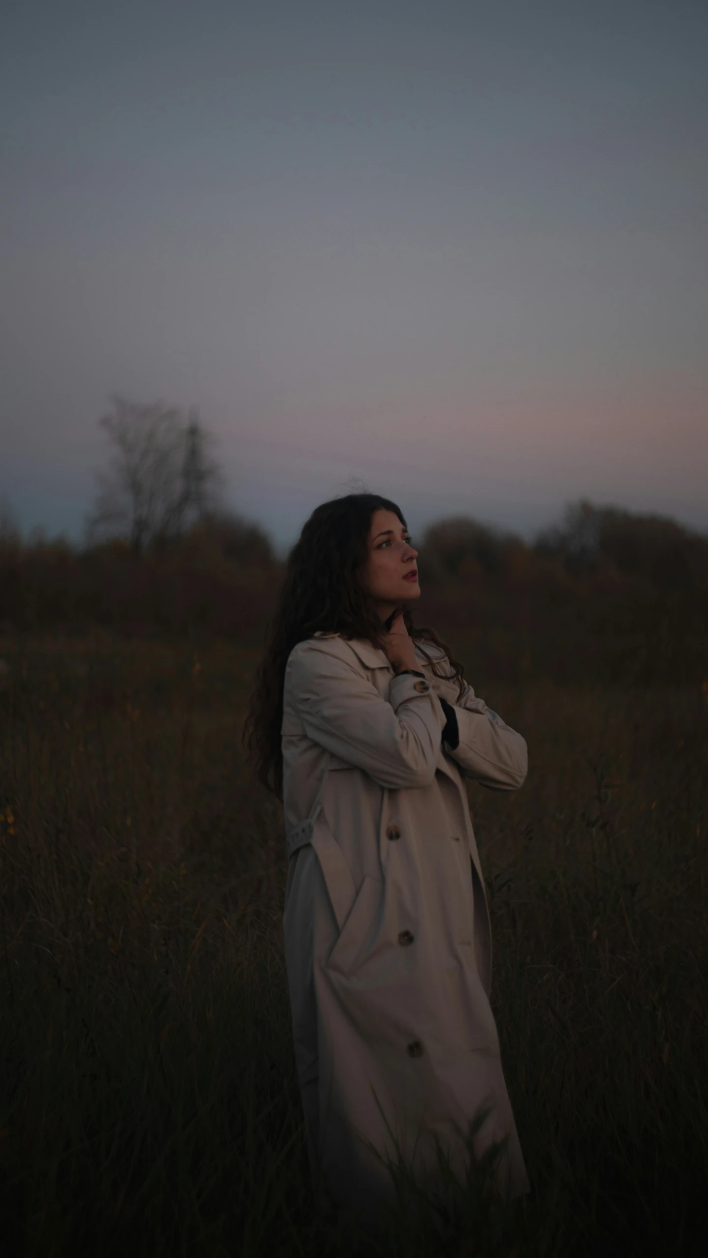 a woman stands in a field with her hands folded to her chest