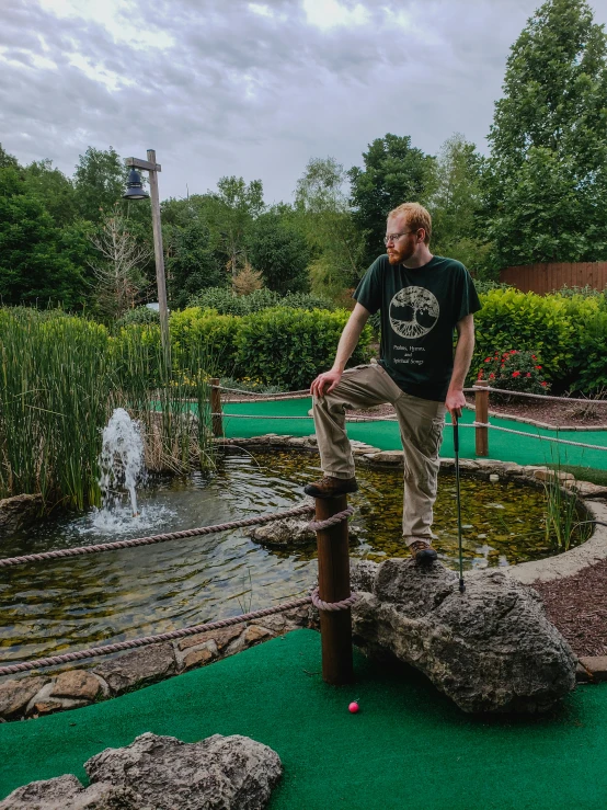 man balancing on wooden post and rope in miniature golf course