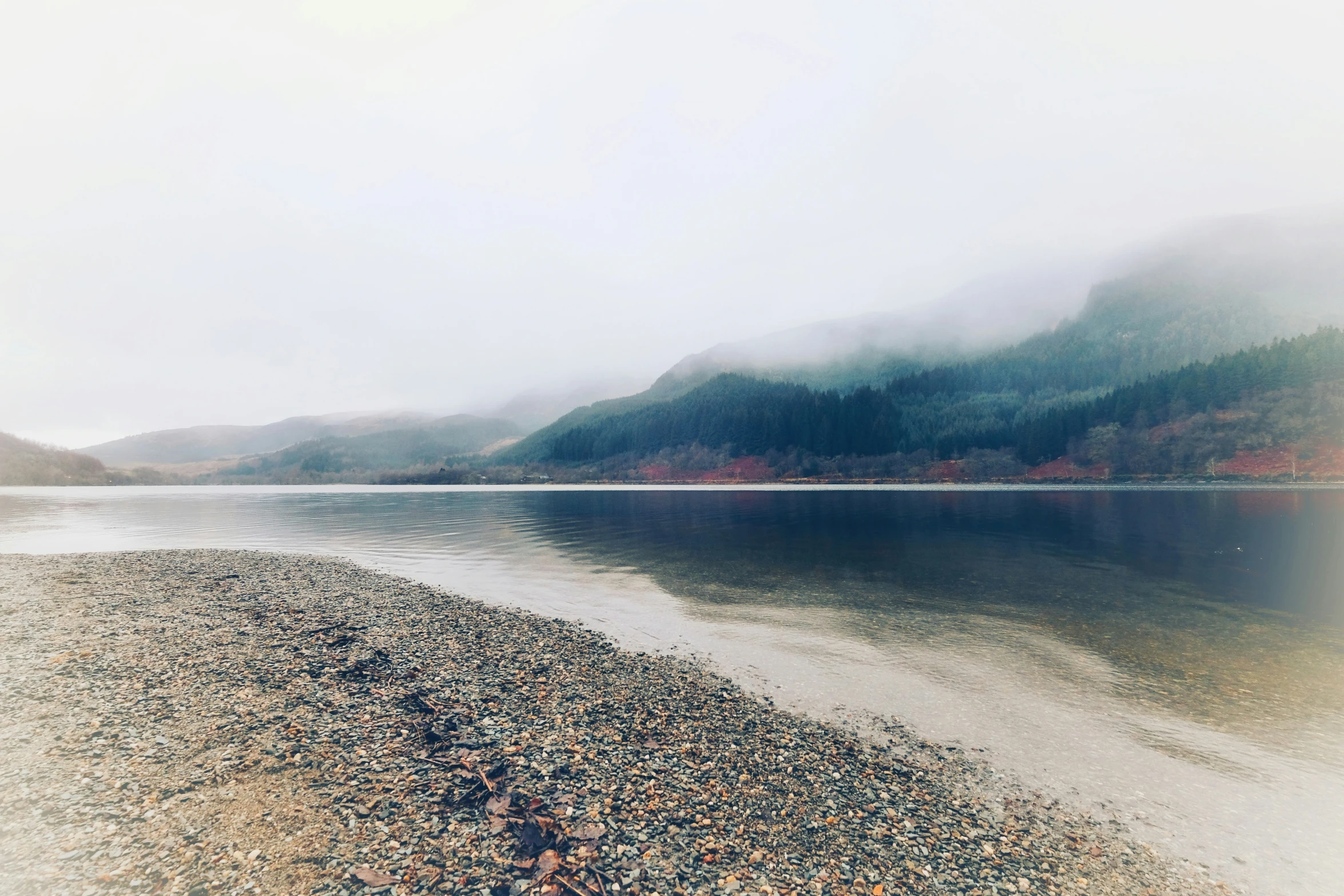 a view of a foggy, misty lake with mountains in the background